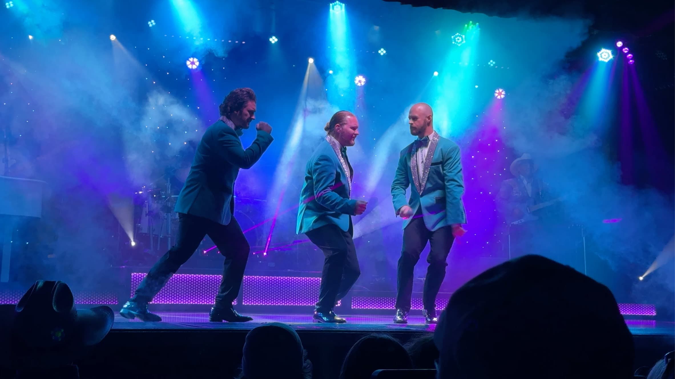 Three performers in blue jackets dancing beneath colorful stage lights during a Branson show
