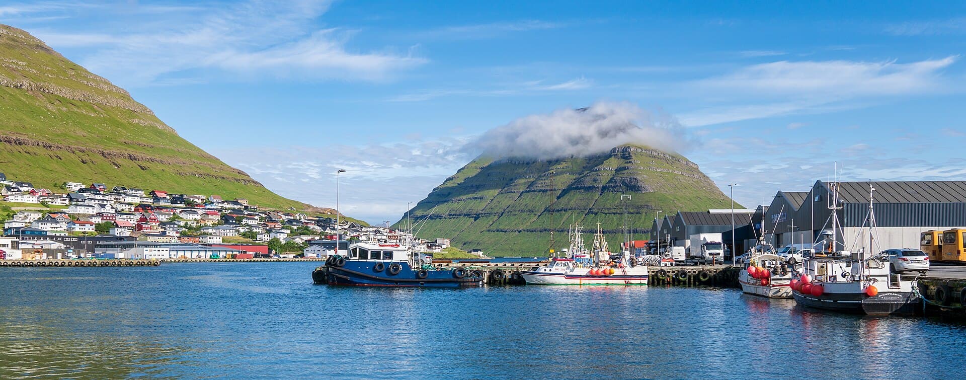 Fishing boats in Klaksvík harbor with mountains behind the town
