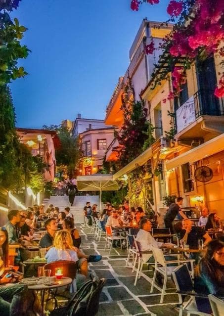 A colorful Athens lane filled with outdoor restaurant tables at night