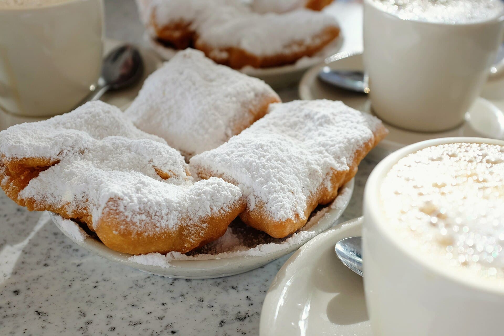 Beignets covered with powdered sugar beside café au lait