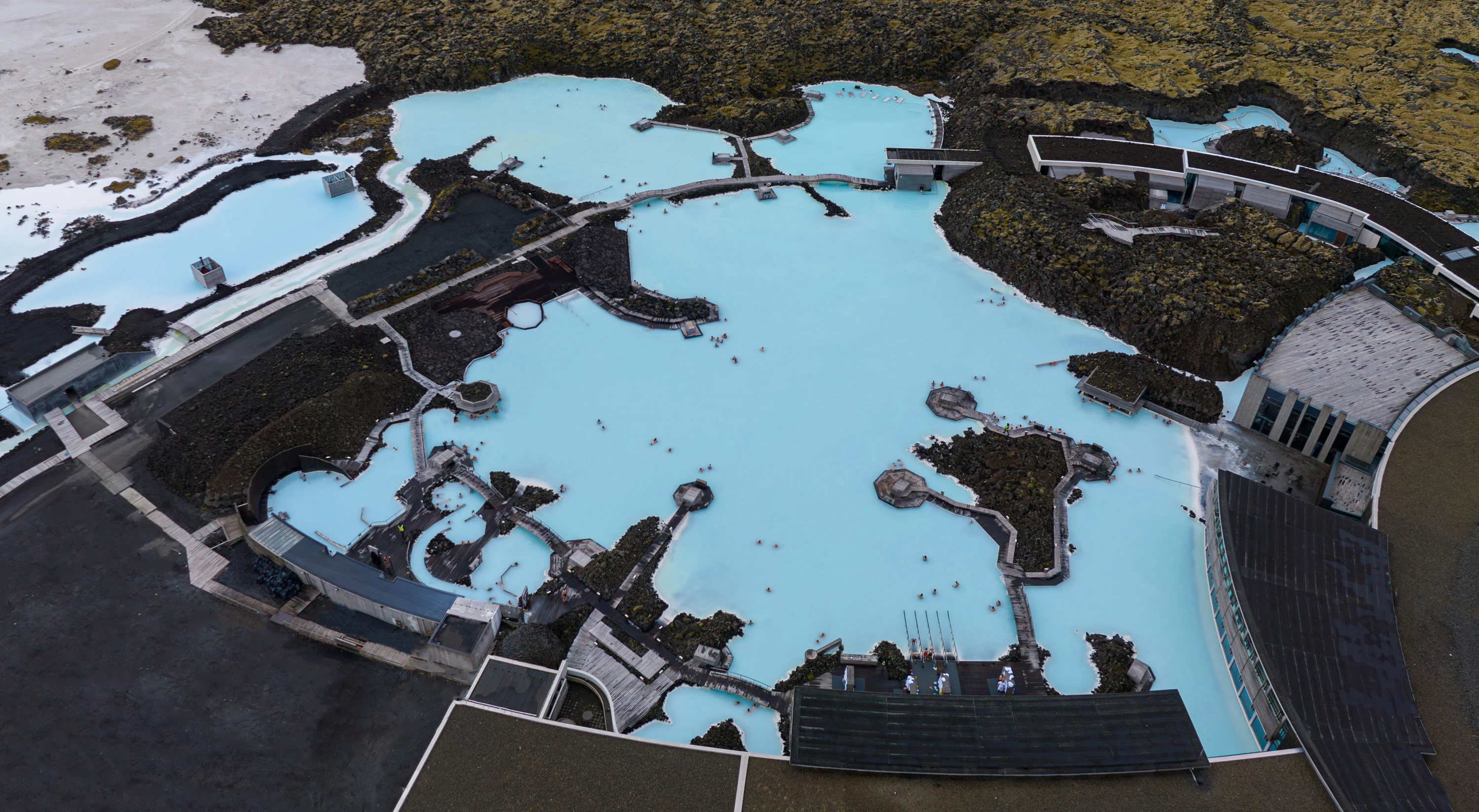 Aerial view of the Blue Lagoon's milky blue geothermal pools, black lava fields, paths, and buildings