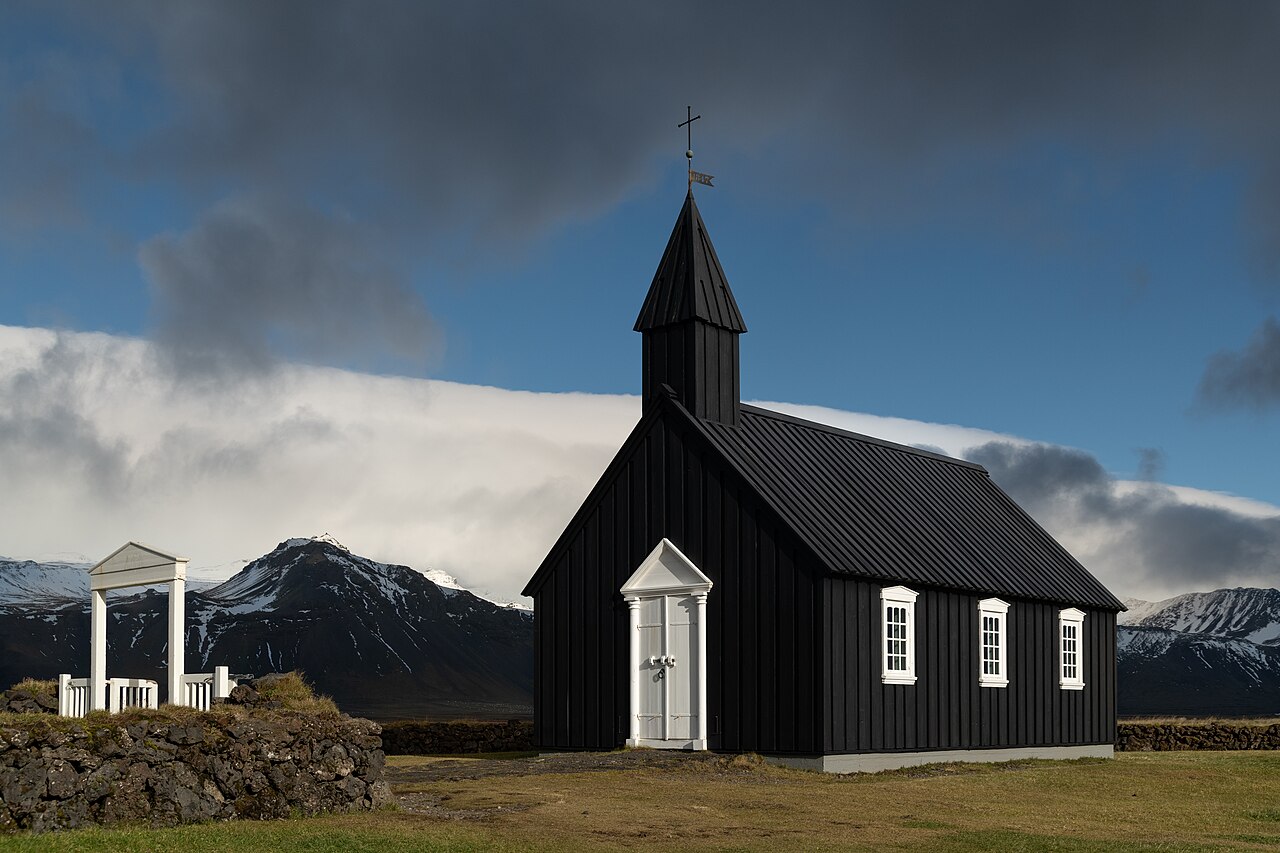 Búðakirkja, a black wooden church, standing before snow-streaked mountains on the Snæfellsnes Peninsula