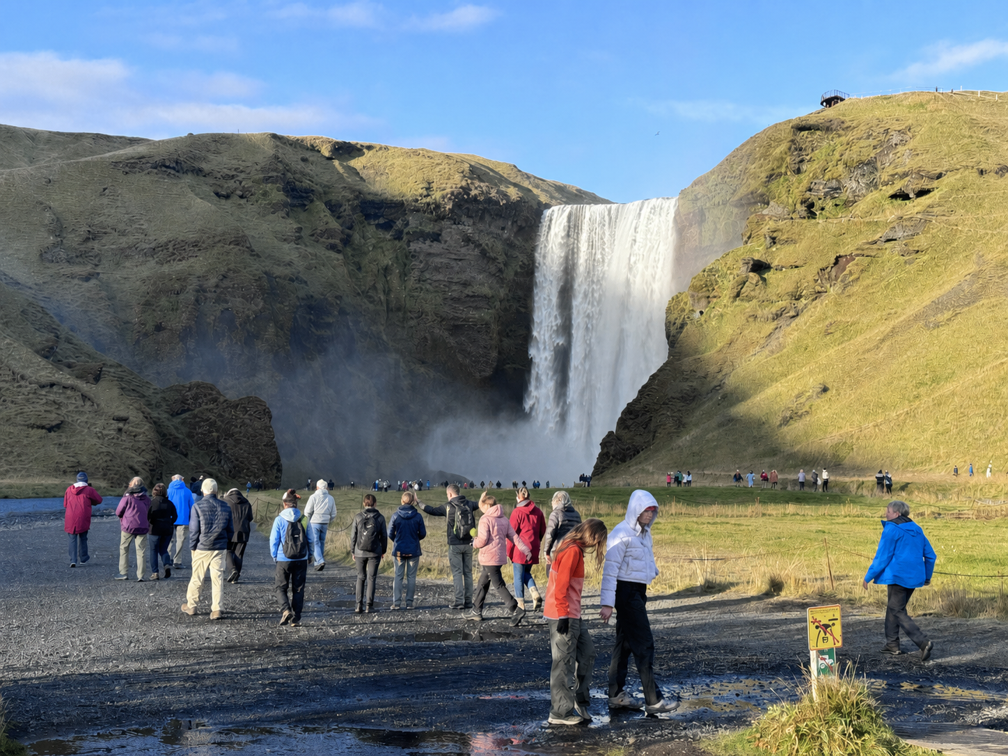 A small group of students walking toward Skógafoss with a guide among other visitors